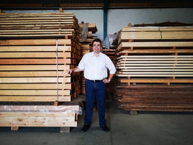 Thomas Ambichl steht zwischen zwei Stapeln geschnittenem Holz